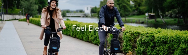 Image of two smiling people riding Brompton electric bikes through a garden