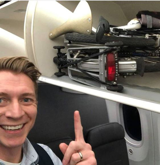 Image of person pointing to folded Brompton bag in overhead compartment on plane