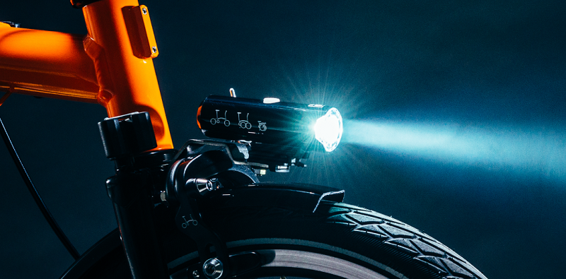 Close up of orange Brompton bike with light shining on front.