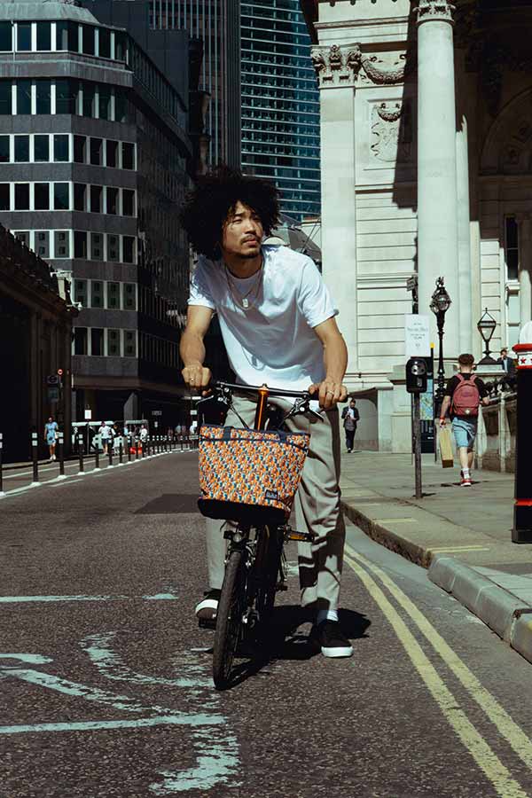 Person riding through London on a Brompton with the Brompton x Liberty tote bag attached to his bike